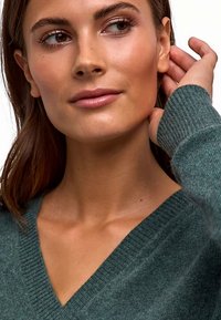 Groene v-hals trui gemaakt van zacht, gestructureerd materiaal; voorzien van geribbelde manchetten en een losse pasvorm die het sleutelbeen omlijst.