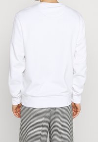 Sudadera blanca de cuello redondo con puños y dobladillo acanalados. Textura lisa, corte regular, vista trasera lisa, combinada con pantalones de pata de gallo en blanco y negro.