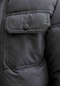 Grå vadderad jacka med en texturerad tyg, en knappad bröstficka och kontrasterande sömmar, som visar upp en modern design.
