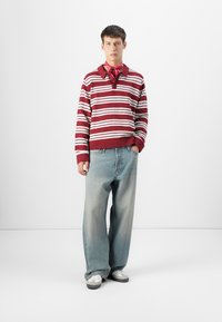 Burgunder- og hvitstripet strikkegenser med krage, kombinert med lyseblå vide denimjeans og grå joggesko, aksentuert med et rødt skjerf.