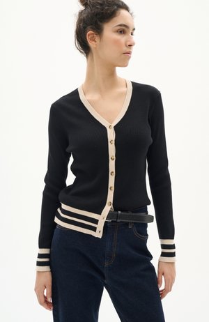 Schwarze gerippte Strickjacke mit V-Ausschnitt und beigem Besatz. Verfügt über goldene Knöpfe und gestreifte Akzente an den Bündchen, kombiniert mit dunklen Jeans.