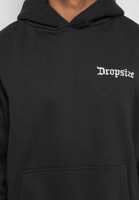 Schwarzer Hoodie aus weichem Baumwollmischgewebe, mit einer Fronttasche und dem weißen, gestickten "Dropsize"-Logo auf der linken Brust.