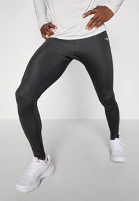 Leggings neri a lunghezza intera realizzati in un materiale liscio e elasticizzato, con un logo discreto sul lato e abbinati a scarpe da ginnastica bianche.