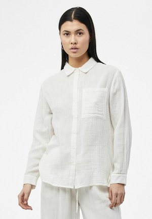 Camisa blanca de manga larga con botones, fabricada en tela texturizada, con collar y un bolsillo en el pecho. Presenta un corte relajado y un dobladillo curvado.
