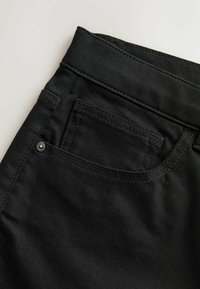Jean en denim noir montrant la partie haute avec la ceinture, la boucle de ceinture, la poche avant et la petite poche à monnaie avec détail de rivet métallique.