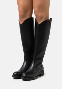 Black leather knee-high boots with a slightly pointed top, side zipper, and flat rubber sole featuring a textured tread pattern.