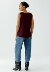 Burgundy sleeveless top with a rounded neckline paired with loose blue denim jeans and black ankle boots with pointed toes.
