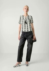 Blusa verde claro con patrón de hojas negras, cuello redondo y mangas cortas, combinada con pantalones vaqueros de pierna ancha negros y zapatos metálicos plateados.
