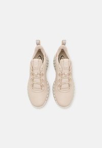 Scarpe da ginnastica beige con superiore testurizzato e colletto imbottito. Presentano un design con lacci e una suola bianca spessa.