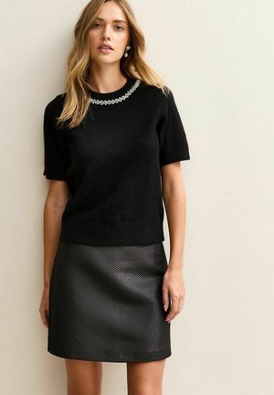 Suéter negro de manga corta con un escote decorado con joyas, combinado con una falda negra acampanada texturizada con rayas diagonales.