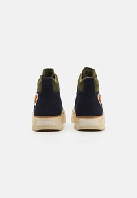 Marineblauwe suède hoge sneakers met groene stoffen accenten, beige rubberen zolen en Sorel-branding op de hiel. Heeft een gestructureerde bovenkant.