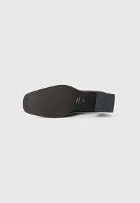 Black leather shoe with a smooth finish, a squared toe, and a low block heel. The sole has ribbed detailing for traction.