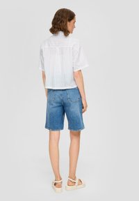 Witte blouse met korte mouwen en gaatjesdetail, gecombineerd met blauwe denim shorts, met een relaxte pasvorm en afgewerkte zoom.