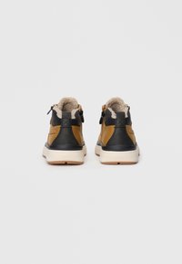 Chaussures montantes marron et noires avec une doublure en peluche beige, des zips dorés et une semelle en caoutchouc blanche. Cuir texturé avec un talon plat.