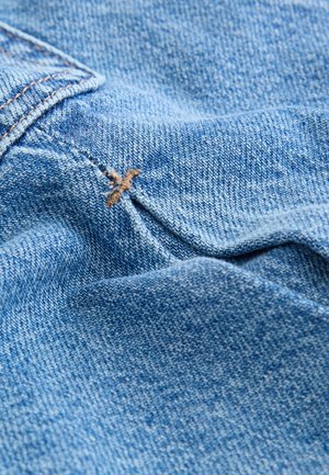 Jasnoniebieska tkanina dżinsowa zbliżenie, z widoczną tkana teksturą i kontrastującym brązowym przeszyciem. Gładka, lekko pognieciona powierzchnia.