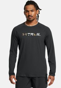 Langærmet sort skjorte lavet af blødt stof med "TRAIL" logo i grå og guld, med rund halsudskæring og raglanærmer.