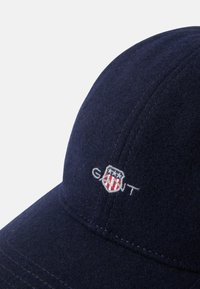 Navy wool cap with stitched seams, featuring a white and red embroidered logo on the front, rounded crown, and curved brim.