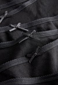Close-up of black fabric with decorative scalloped edges and small black ribbon bows sewn in a row.
