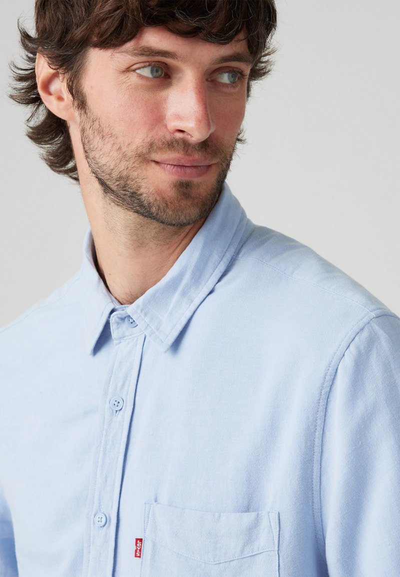 Lichtblauwe button-up overhemd van katoen, met een kraag, een borstzak en een klein logolabel op de zak. Soepele textuur.