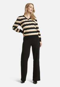 Black and cream V-neck sweater with zigzag pattern, long sleeves, and ribbed hem; paired with black, fitted trousers and heeled shoes.