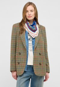 Brązowa w kratę dwurzędowa marynarka z czerwonymi i niebieskimi akcentami, w połączeniu z dżinsową koszulą i wzorzystym szalikiem, o luźnym kroju.