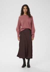 Suéter rosa claro acanalado combinado con una falda midi marrón oscuro con lunares blancos. Se lleva con botines negros de tacón.