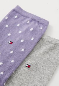 Due paia di calzini sono esposte: un paio lavanda con pois bianchi e un paio grigio con un piccolo logo rosso, bianco e blu.