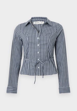 Marineblå og hvit rutete skjorte med lange ermer, knappet foran, justerbar knyting i midjen og spiss krage. Bomulls materiale.