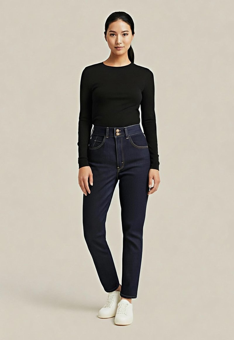 Jean taille haute bleu foncé avec des détails en bouton et en couture dorés, associés à un haut noir à manches longues et des chaussures blanches sur un fond neutre.