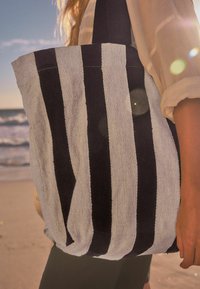 Gestreepte tote bag gemaakt van zachte stof, met afwisselend marineblauwe en lichtgrijze strepen, stevige handvatten en een gestructureerd oppervlak.