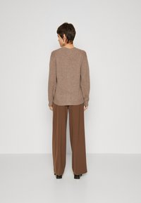Brown knitted sweater with a relaxed fit, long sleeves, and side slits, paired with wide-leg brown trousers and black heel boots.