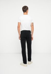 Jeans neri in denim con vestibilità slim, cinque tasche e vita media, abbinati a una semplice t-shirt bianca a maniche corte e scarpe da ginnastica chiare.