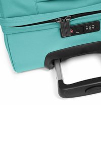 Turquoise koffer met zwarte hardware, voorzien van dubbele ritsen, combinatie slot en uitschuifbare zilveren handgreep. Textuur op de oppervlakte van de stof.