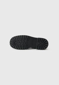 Semelle de chaussure en caoutchouc noir avec des semelles profondes et des motifs croisés pour l'adhérence, dotée d'un bord lisse. Design minimaliste et matériau durable.