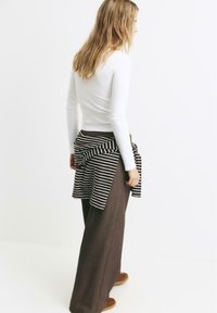 Top alb cu maneci lungi, pantaloni maronii cu croi larg si o fasa cu dungi alb-maro legata in talie. Tesatura fina si croi lejer.