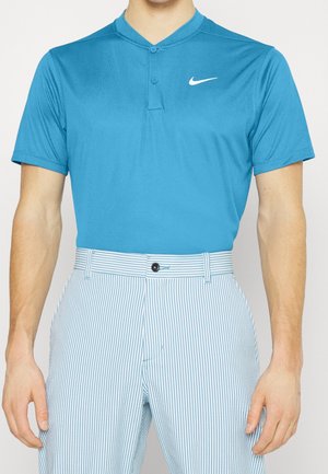 Homme portant un polo Nike bleu à manches courtes avec une patte à deux boutons et un pantalon rayé bleu et blanc taille haute.