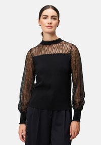 Schwarzer Pullover mit semitransparenten, strukturierten Spitzenärmeln im Fischgrätmuster und einem hohen Halsausschnitt mit rüschigem Rand.