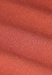 Textilstoff in einem warmen Korallton, mit glatter Textur und feinem Webmuster, das sanft mit zarten Falten fällt.