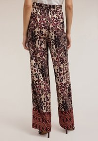 Wijdvallende broeken met een bloemenprint in bordeauxrood en crème kleuren. Elastische tailleband en gestikte zoom in rijke rode tinten.