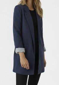 Granatowa marynarka z otwartym przodem, długimi rękawami i podwiniętymi mankietami w paski. Wykonana z gładkiej tkaniny, o luźnym kroju i bocznych kieszeniach.