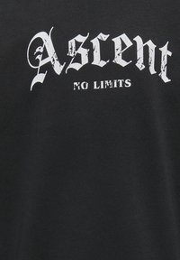 Camiseta negra de algodón, con un gráfico desgastado en blanco que presenta el texto "Ascent NO LIMITS" en una fuente en negrita y estilizada.