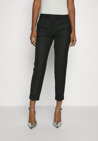 Black tailored pants with a cuffed hem, featuring a flat front design and a smooth texture. Paired with silver strappy heels.