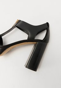 Sandale negre cu toc înalt, realizate din piele netedă, cu un design decupat, având un fermoar metalic și un toc pătrat robust.