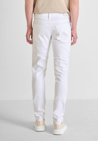 Pantaloni in denim bianco con vestibilità slim, dotati di tasche posteriori e vita media. Il tessuto ha una texture liscia e un design pulito.