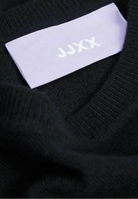 Svart stickad tröja med mjuk textur, med en lavendelfärgad etikett som visar "JJXX" i vit text.