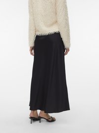 Camisola cremosa e felpuda com mangas compridas, combinada com uma saia maxi de cetim preta. O conjunto inclui sandálias pretas de salto.