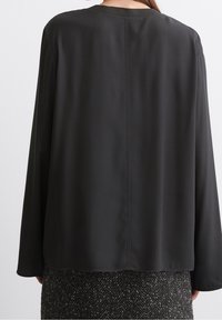 Blusa nera a maniche lunghe realizzata in un tessuto leggero e morbido; presenta un colletto rotondo e una cucitura centrale sul retro.