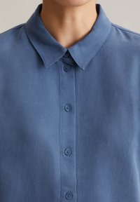 Blaues Hemd mit Knopfleiste, das aus einem strukturierten Stoff gefertigt ist, einen klassischen Kragen hat und über drei Knöpfe an der Knopfleiste verfügt.