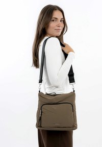 Ciemnobrązowa torebka typu crossbody wykonana z pikowanej tkaniny, z zamykaną na zamek przednią kieszenią oraz czarnym paskiem z metalowymi akcentami.