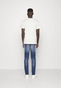 Camiseta de algodón blanca, de manga corta, combinada con jeans de mezclilla azul, de corte ajustado, lavado claro, terminada con zapatillas blancas.